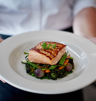 Photo of salmon entree on a plate, held by staff member