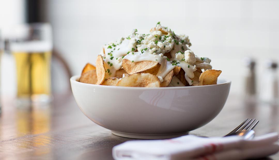 A photo of hot potato chips topped with blue cheese fondue, crumbled blue cheese, and chives