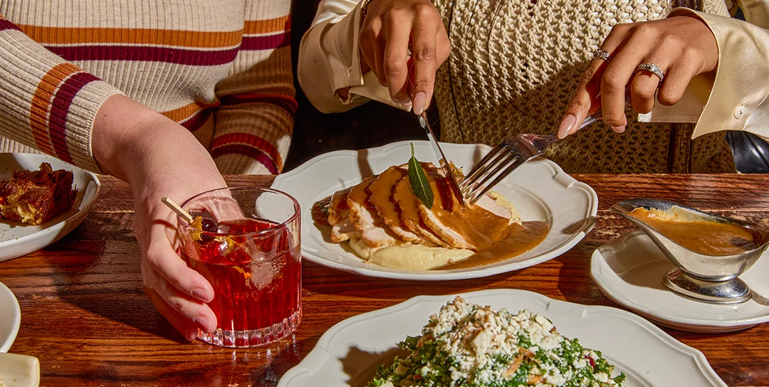 Two people sitting at a table with a cocktail and turkey breast for Thanksgiving